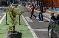 pedestres atravessam em faixa em rua estreitada por extensões de meio-fio