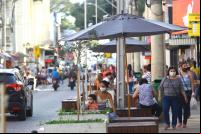 foto de uma rua em São José dos Campos. Pessoas conversam sentadas sob ombrelones na calçada. Carros am lentamente na rua.