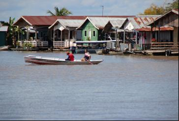 homem e mulher navegam de barco em frente a casas na beira de rio