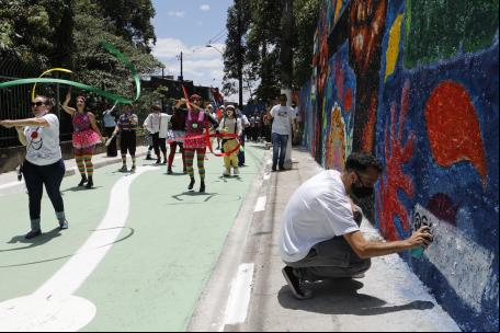 homem pinta muro enquanto pessoas am por rua colorida