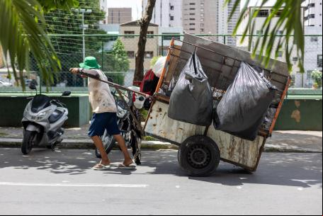 Um homem puxa um grande carrinho cheio de lixo.