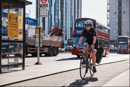 mulher de bicicleta em rua de Londres com ônibus típico ao fundo