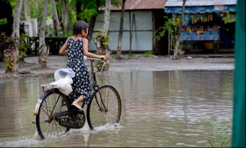 Menina pedala bicicleta em área alagada