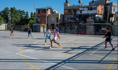 Crianças jogando futebol em uma cancha em meio a casas simples
