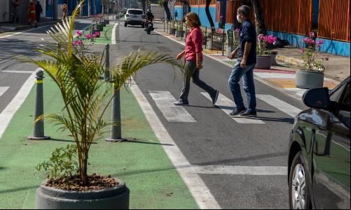 pedestres atravessam em faixa em rua estreitada por extensões de meio-fio