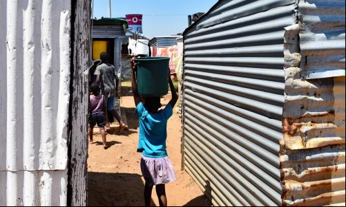 Menina carrega água em favela de Joanesburgo