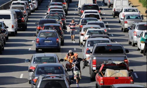vendedores ambulantes em meio a carros em congestionamento