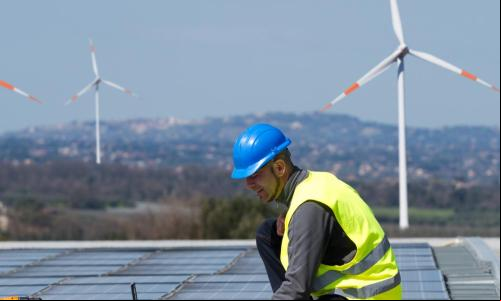homem durante instalação de solar com estações de energia eólica ao fundo